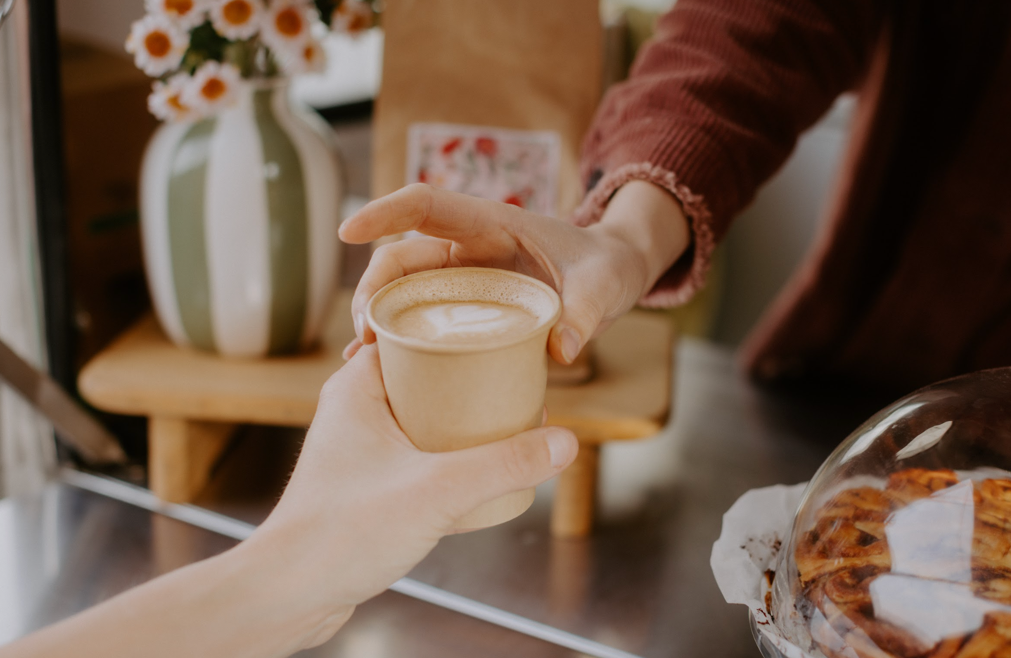 Een Cappuccino met hartjes latteart wordt uitgegeven vanuit de koffiebar met JUNE Santos N01 Koffiebonen op de achtergrond
