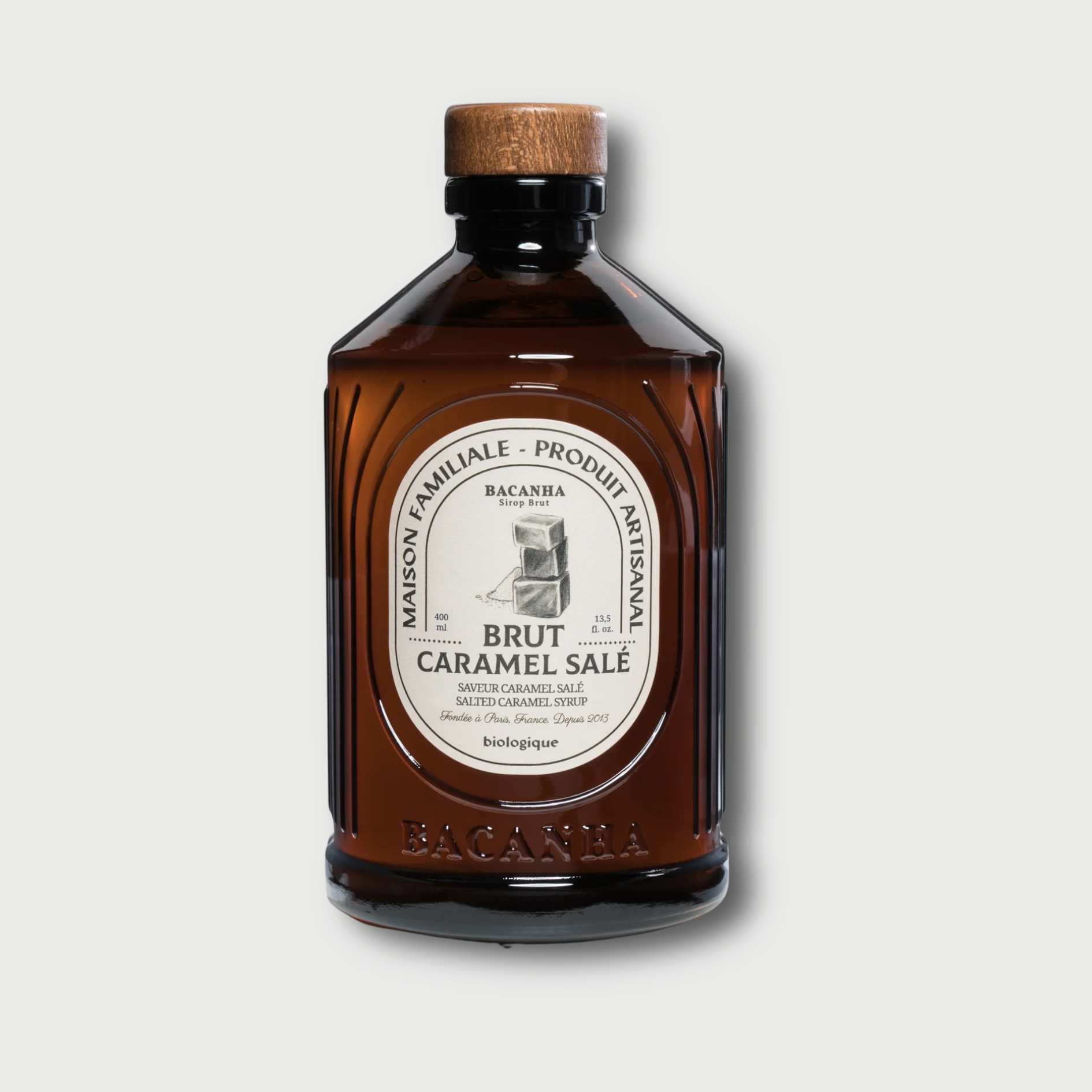 Brown Bacanha Salted Caramel bottle with a wooden cap on a light gray background