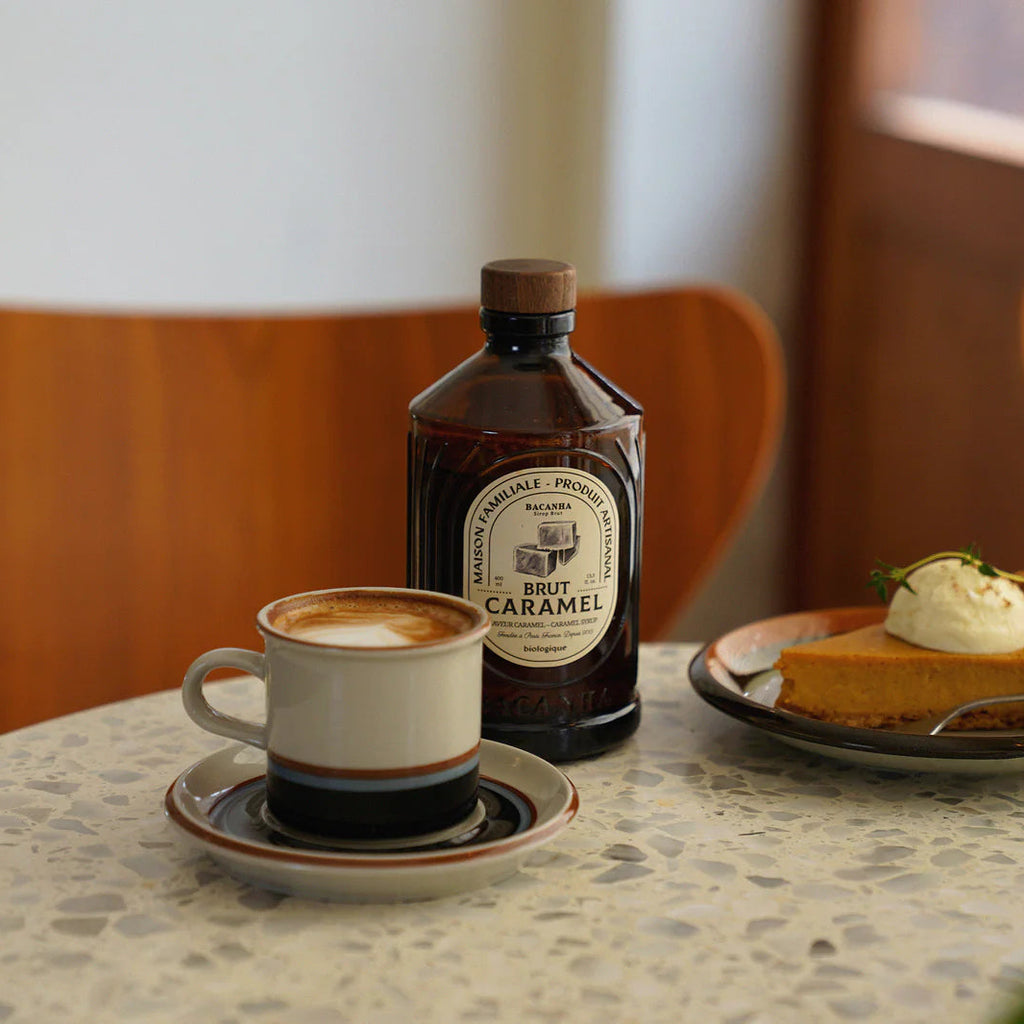 Brown bacanha brut caramel sirup bottle with wooden cap on a stone table with a pumpkin pie and cappuccino besides it