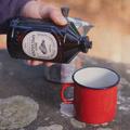 Bruine glazen bacanha speculoos siroop fles met een houten dop op een lsteen gegoten in een rode mok met een percolator